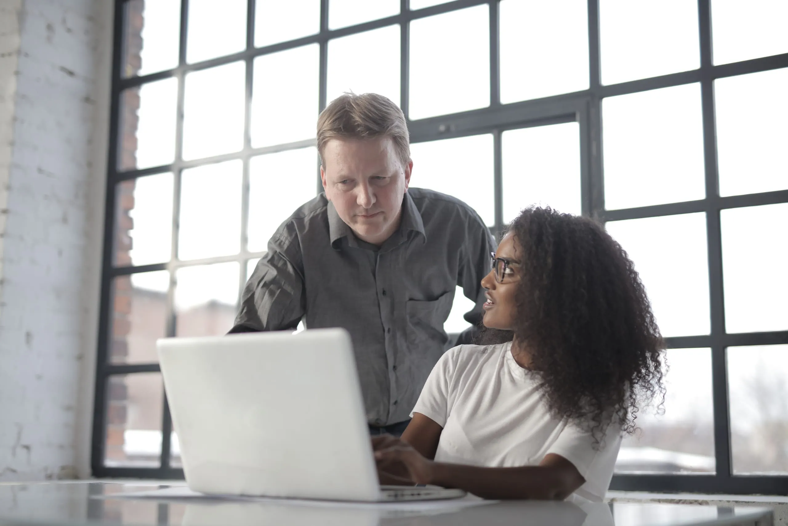 Un formateur accompagne une apprenante devant un ordinateur portable pendant une formation tutorale
