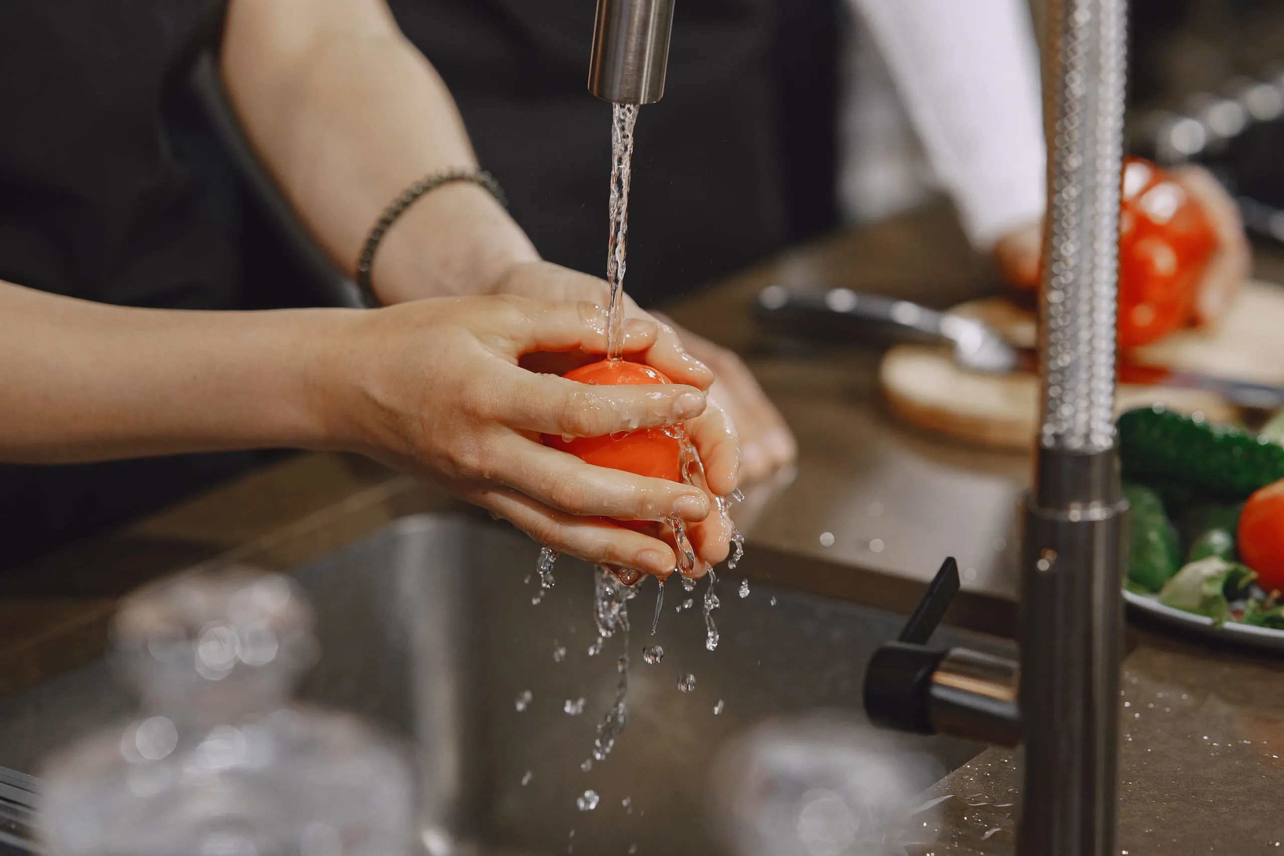 Lavage d'une tomate sous un robinet dans une cuisine professionnelle