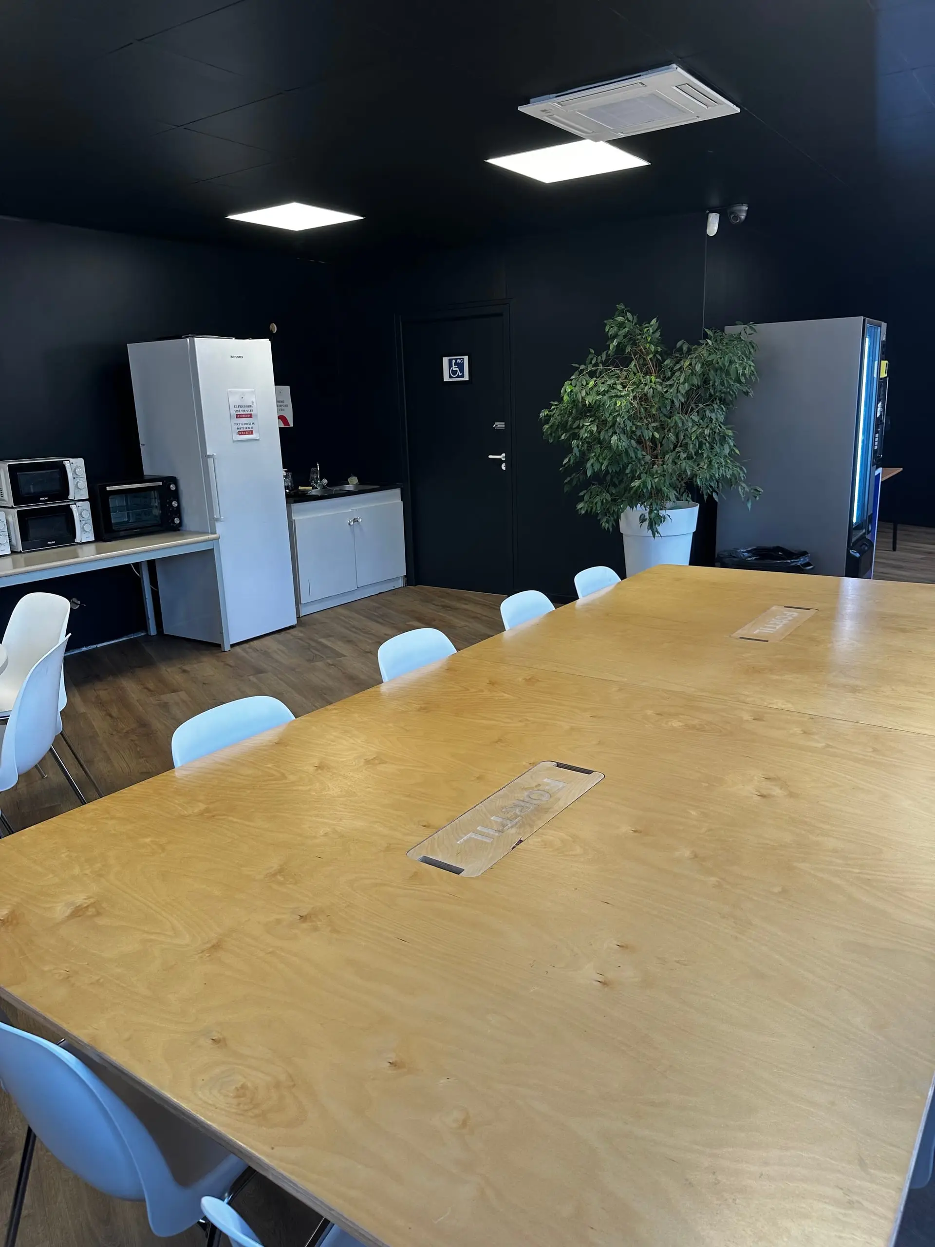 Salle de pause du CFA Paedagogia avec grande table, coin cuisine et décoration végétale