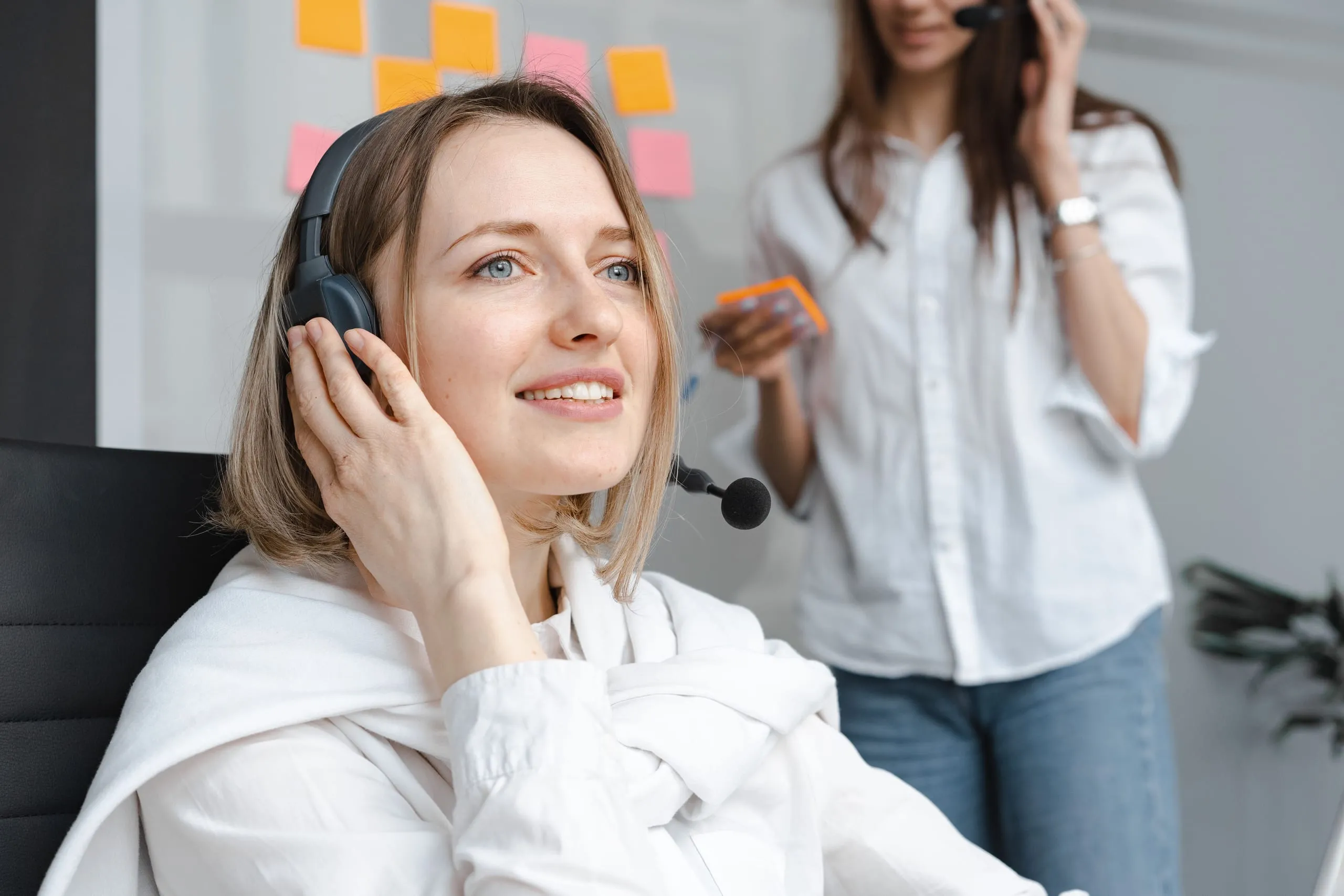 Professionnelle portant un casque-micro en situation d’écoute, avec une collègue en arrière-plan