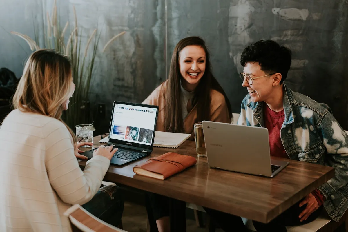 Trois jeunes apprenants autour d'une table avec des ordinateurs portables, engagés dans une session de travail collaboratif