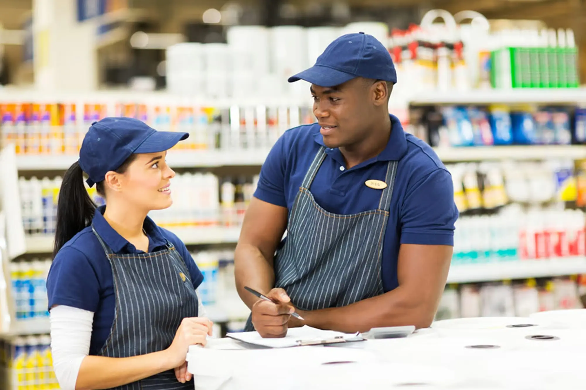 Manager d'établissement marchand en uniforme bleu supervisant un collaborateur au comptoir